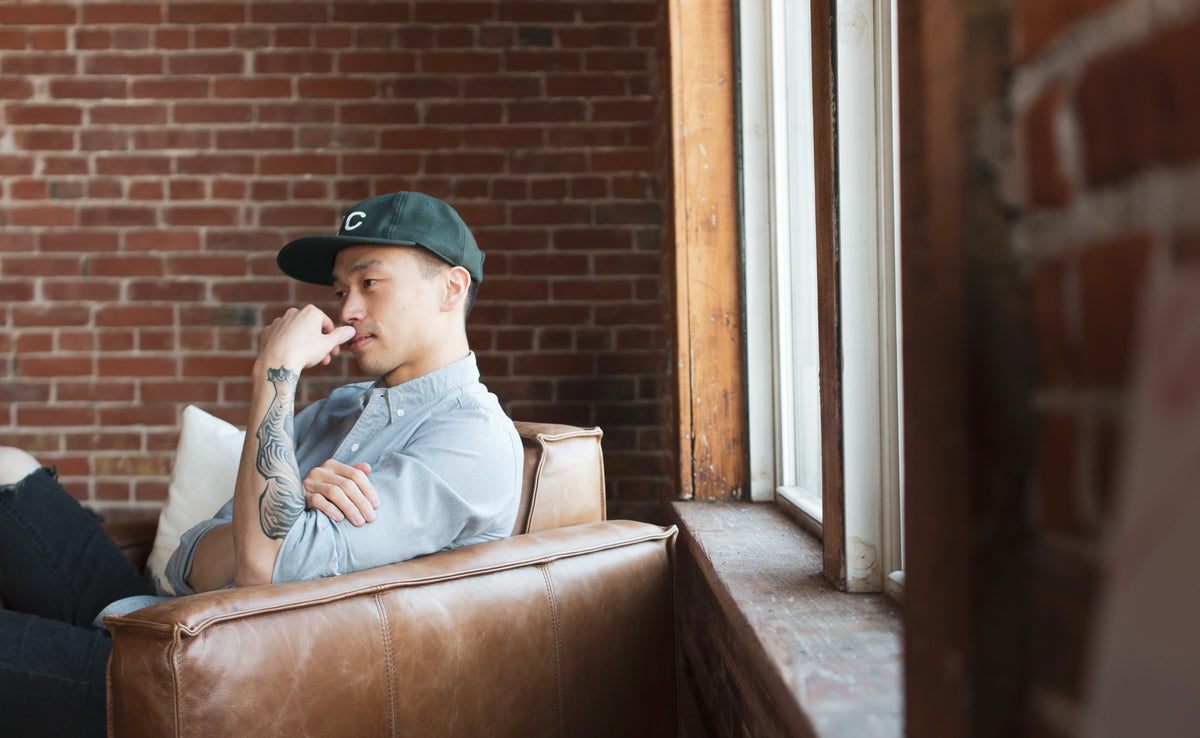 Person wearing a green Sandlot baseball cap seated beside a window